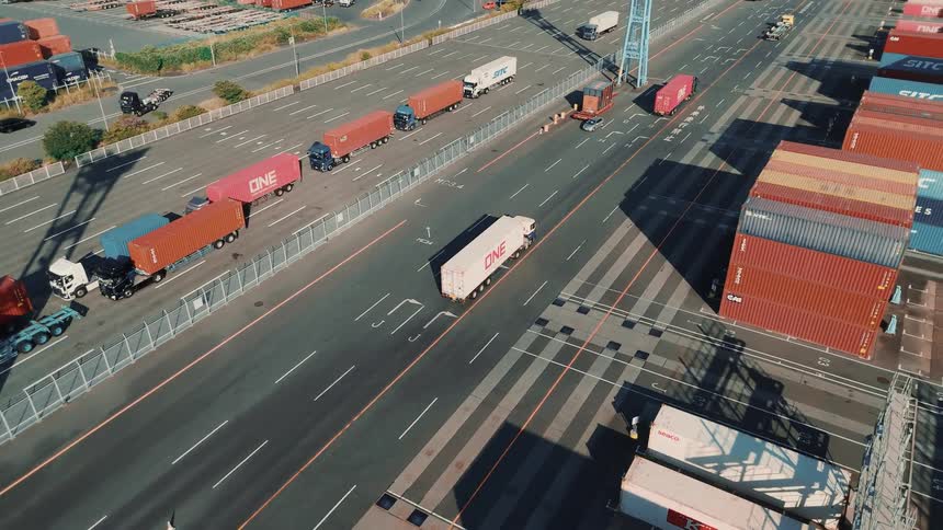 Trucks transport shipping containers beside organized stacks in a port terminal