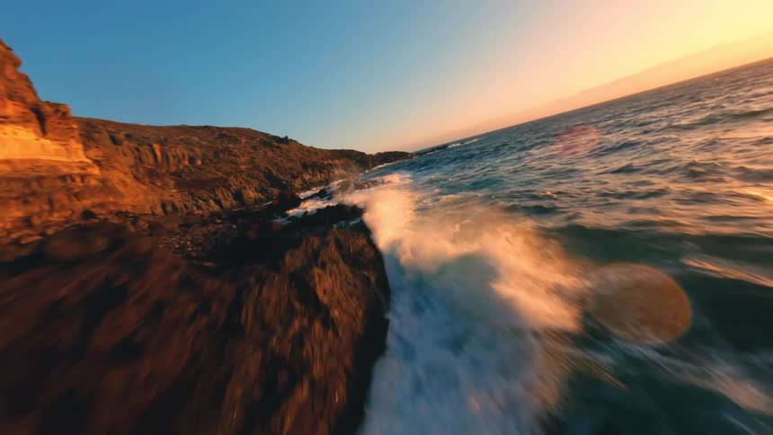 Flying fast over a rocky coast with the sea waves hitting the rocks with force