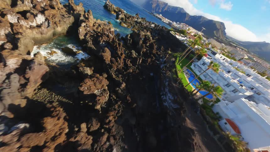 Flying fast over a rocky coastal cliff under a summer resort