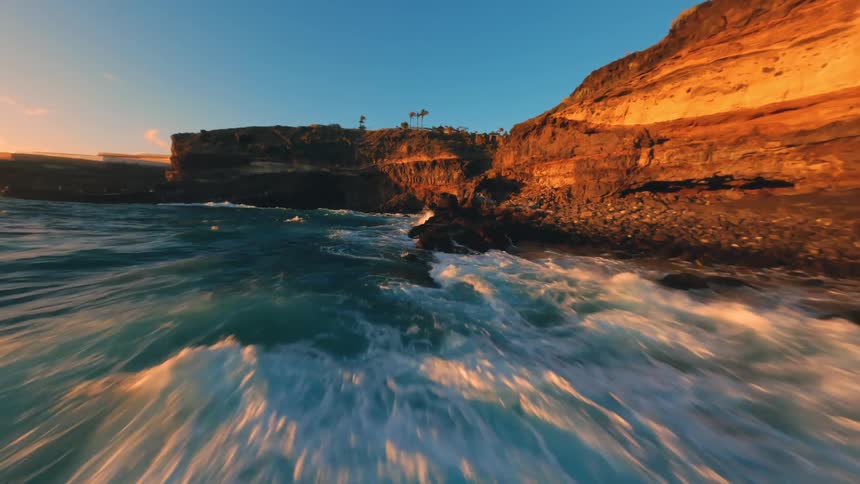 Flying fast over a rocky coast with the sea waves hitting the rocks with force