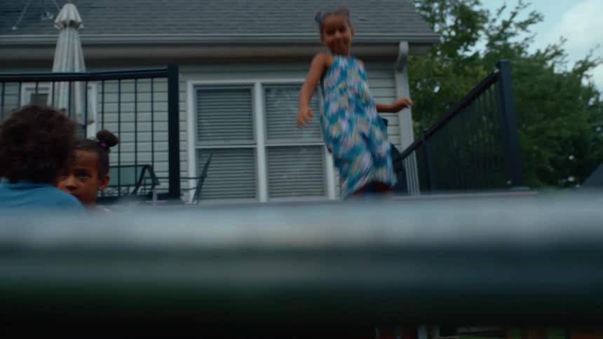 Biracial male and female children playing on a trampoline on a lawn with a house on the background outdoors during day time