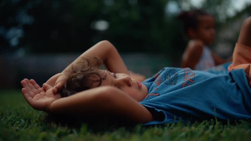 A boy and a girl are lying on grass and theres a third girl sitting on the grass all in an outdoor setting