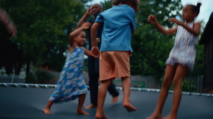 A group of adults and children jump on a trampoline outdoors