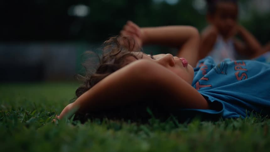 Child lying on a grass lawn at midday wearing a blue shirt