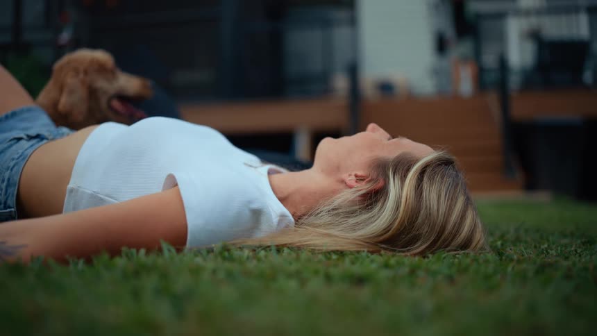 A woman lies on a lawn with a dog next to her