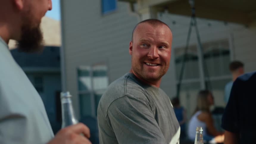 Three men are smiling and holding drinks outdoors at a social gathering