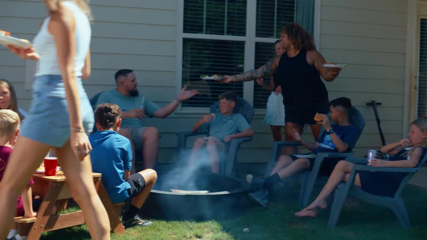 A group of people of all ages is eating and relaxing in a backyard on a sunny day