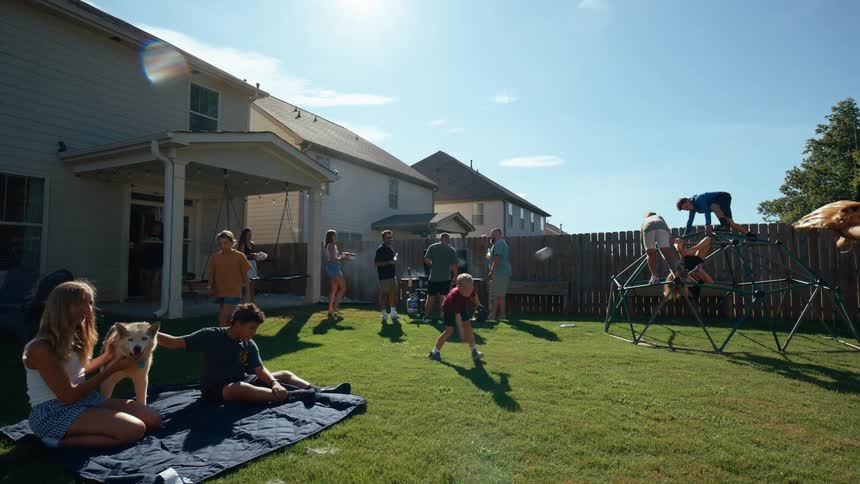 Families and kids enjoy a sunny backyard gathering with people grilling children climbing on a jungle gym and others sitting on a blanket with a dog