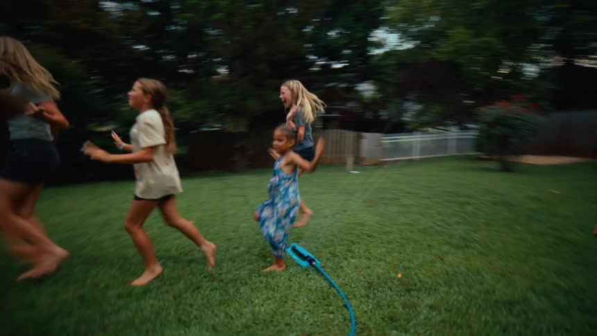Children and a dog play together in a backyard with a sprinkler on