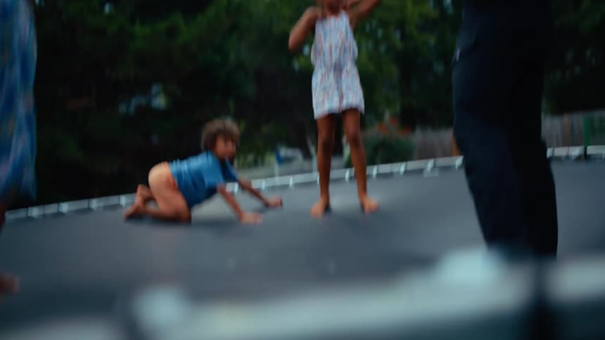 Father with son and two daughters playing on a trampoline on a lawn outdoors