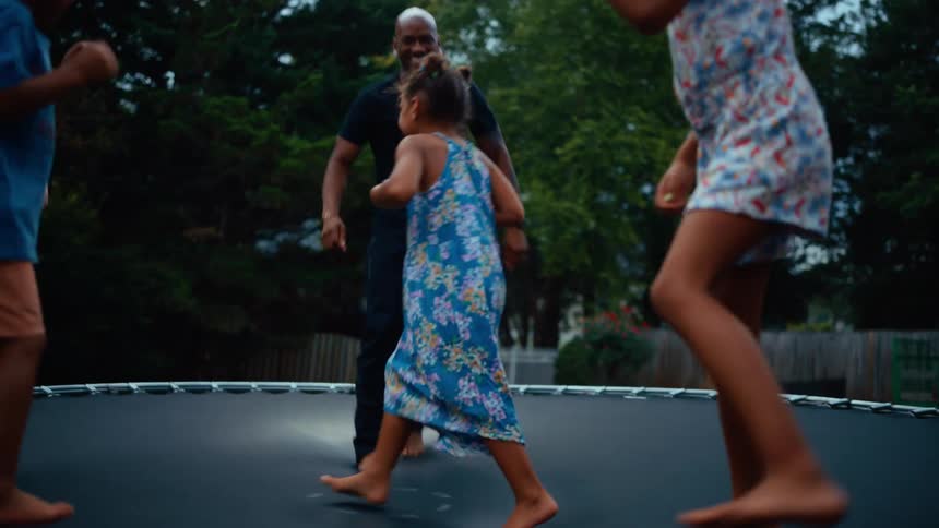 A diverse group of adults and children joyfully bounce on a trampoline outdoors