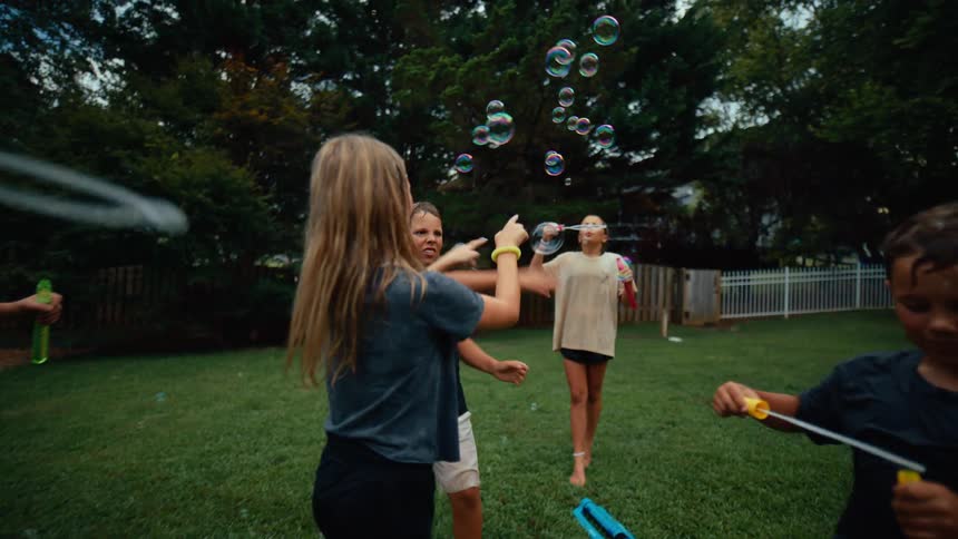 Small group of children and teenager playing with bubbles on a lawn outdoors during day time