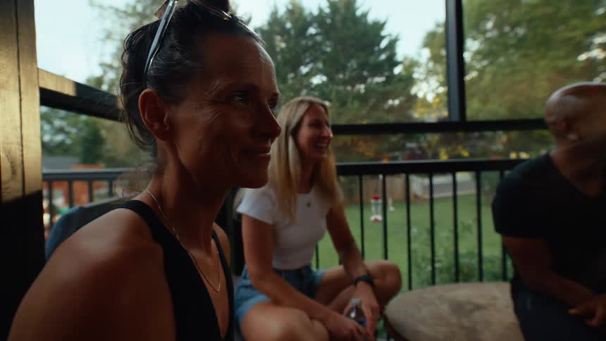 Three friends sit together in an outdoor area at midday chatting and laughing under the bright sun enjoying each others company in a relaxed cheerful atmosphere