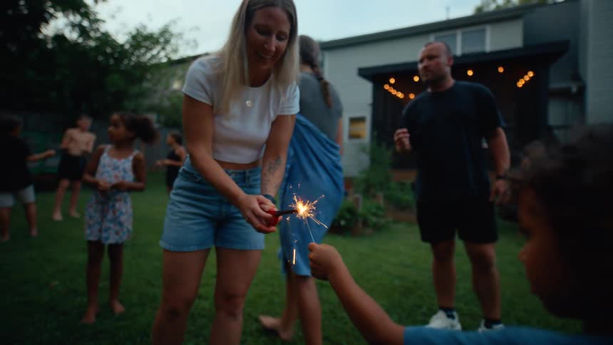 A lively midday backyard gathering where family and friends enjoy time together on a sunny lawn kids laugh and play some holding small discostyle fireworks that sparkle in the daylight while adults chat relax and join in the fun