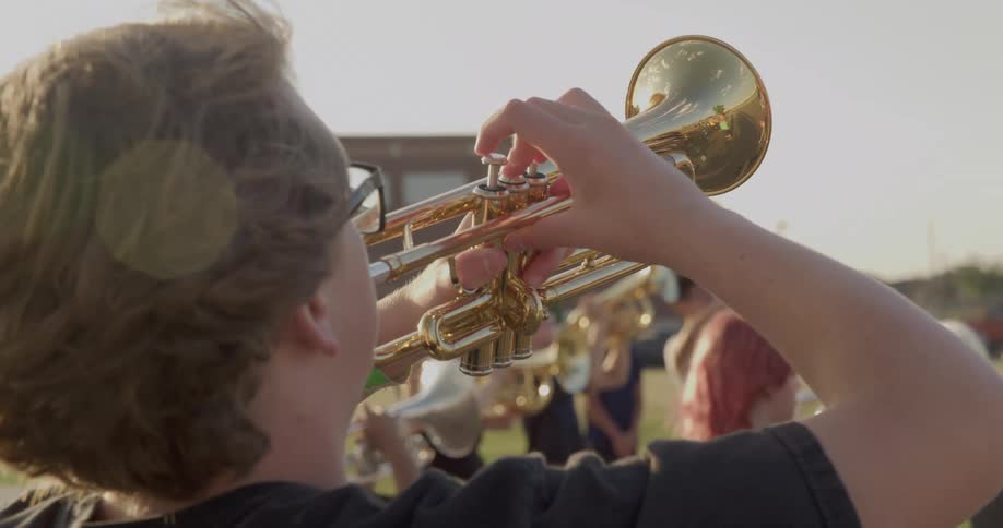 Members of a brass band play while standing in a field on a windy day