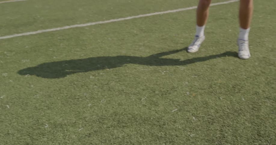 The video shows a lowangle shot of a persons legs walking on a grassy sports field in the foreground there is a white painted line on the grass a second white painted line is also visible in the background running parallel to the first line