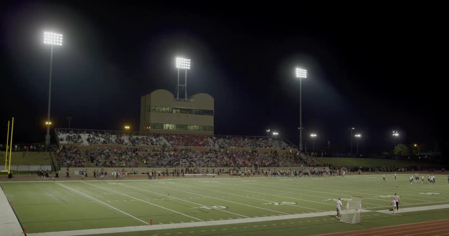 The bleachers are full of football fans at night