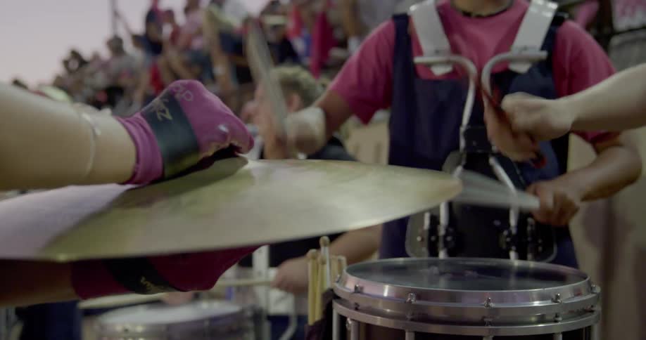 The band is playing drums by the crowd in the bleachers