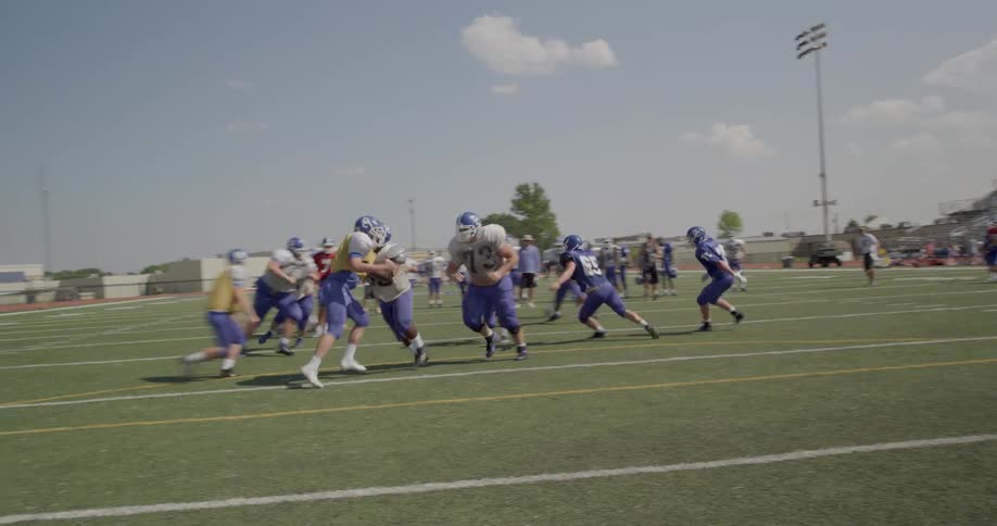 A group of american football players are on the field actively playing a game under clear sunny skies