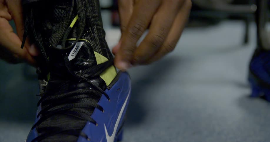 A persons hands are shown tightening the laces of a blue and black athletic shoe