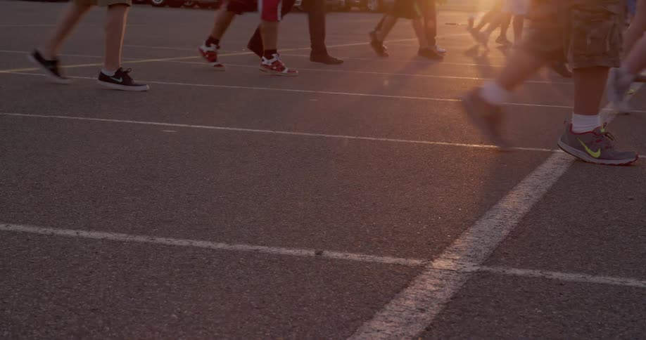 The video shows a group of people walking on a running track in the foreground there are two distinct lines of people walking parallel to each other the camera focuses on their feet and legs as they move along the track