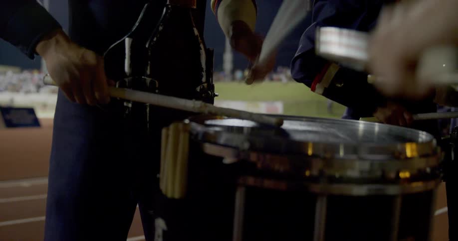 The band members tap their drums on the football field