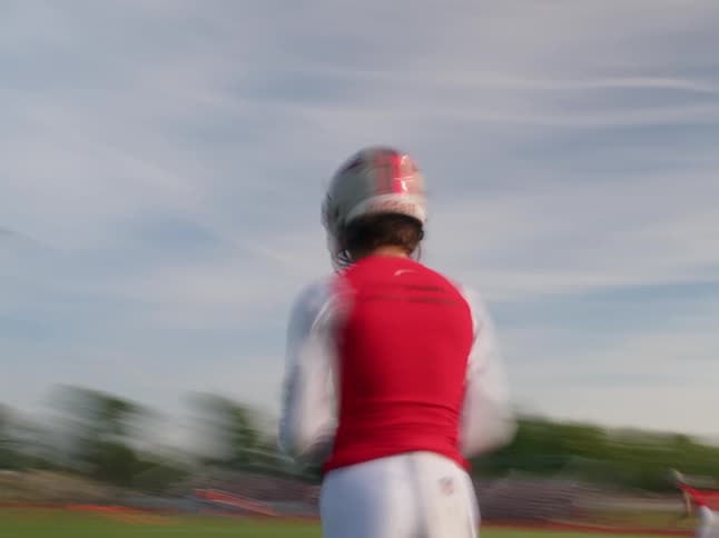 A young male high school football player in a white helmet and red jersey is throwing a ball on a grassy field in an action shot with a slightly blurred background