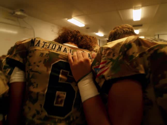 Football players bowing their heads in a huddle in a locker room