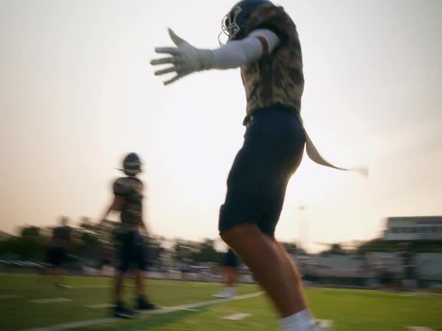An american football player walks onto the pitch at midday shaking his teammates hand in excitement during the game