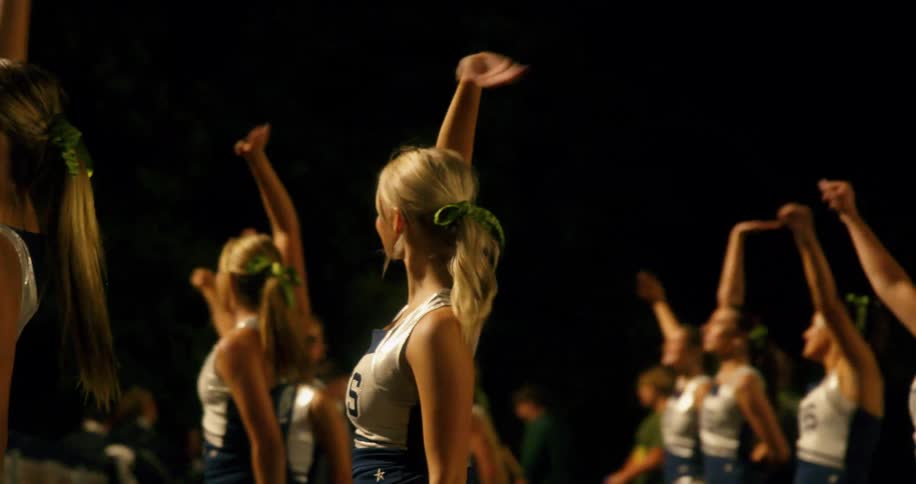 A group of young women cheerleaders performing a routine at night with one woman in the foreground waving