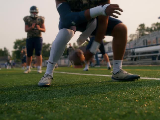 An american football player passes the ball backward to a teammate behind him on the field during a game on a sunny evening the warm light casting long shadows across the turf
