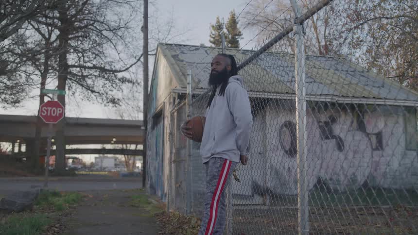 The man is leaning against a fence holding a basketball