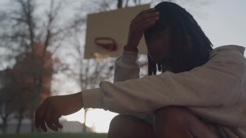 The man is sad while he sits on the basketball court