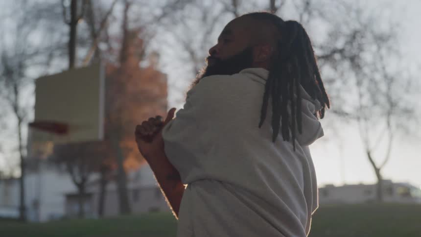 A black man stretches his arms while standing on a basketball court on an autumn day