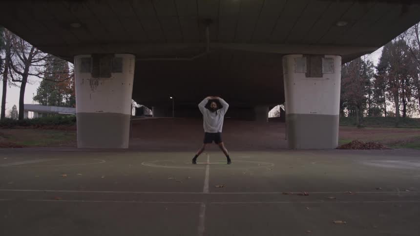 A black man performs jumping jacks while standing under a bridge on an autumn day