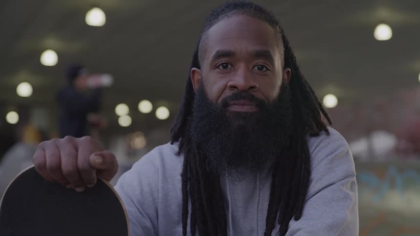 A black man with ling beard and long braded hair indoor holding a container