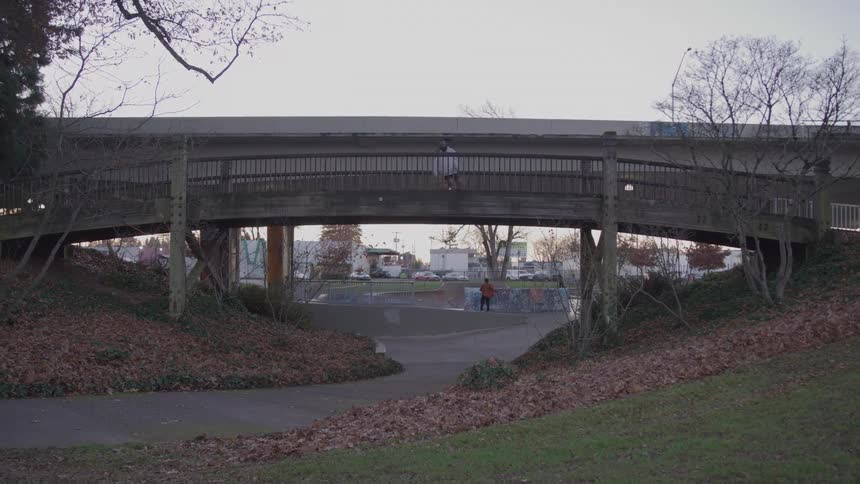 Person on a bridge playing basketball and in the background another person riding a skateboard