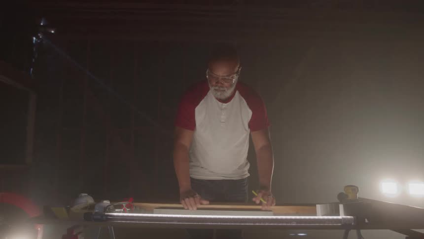 Man wearing safety glasses uses a ruler to measure a piece on a lit workbench