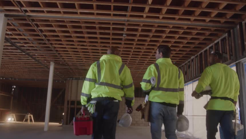 Three man walk into a building while carrying items and wearing clothing