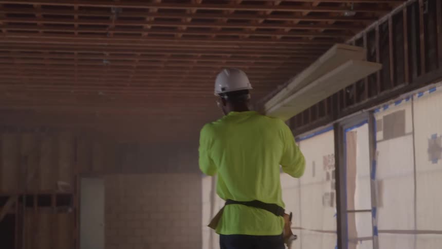 Worker wearing a helmet carries wooden boards on his shoulder at a construction site