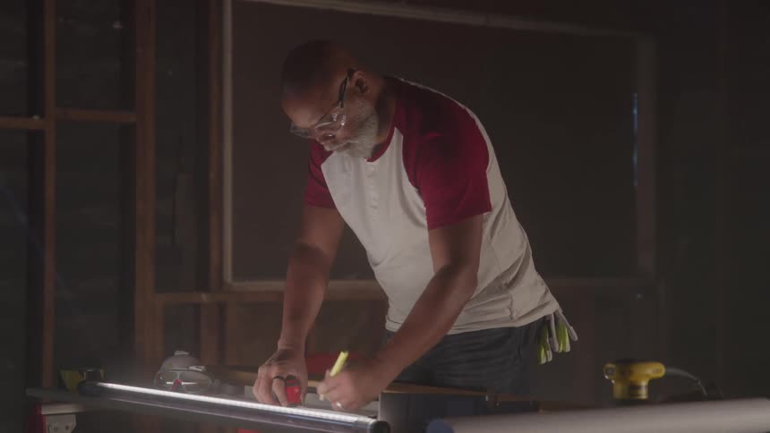 Man wearing safety glasses measures a lit pipe in a workshop