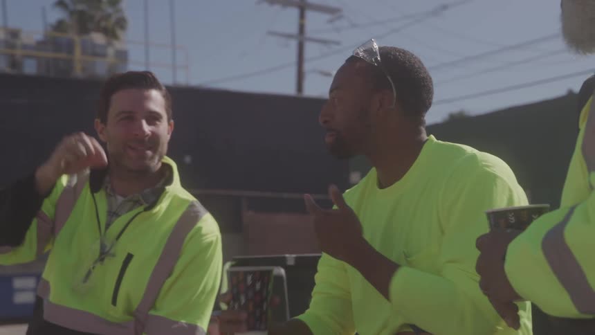 Workers in reflective vests take a break while drinking coffee outdoors