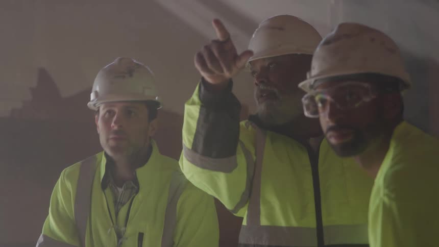 Workers wearing helmets and reflective vests review a project in a construction setting