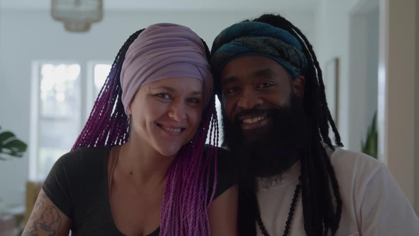Mixedrace couple black and white standing side by side indoors in their living room smiling