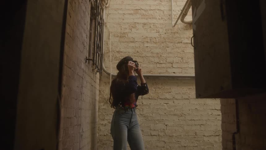 Female photographer standing in a narrow alley smiles while taking a picture