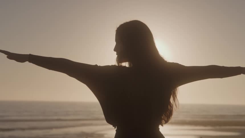 The woman is stretching as the sun rises