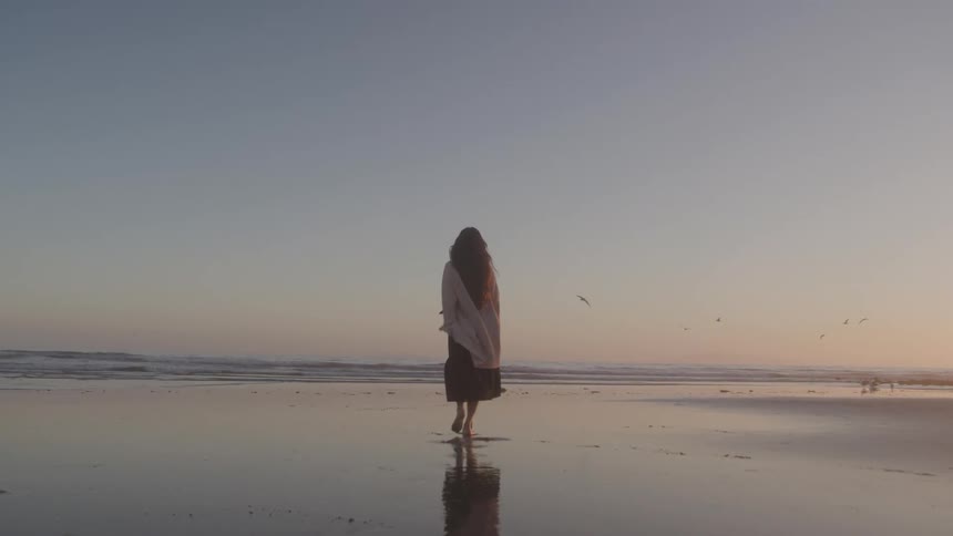 Woman walking calmly on the wet sand of the beach at dawn