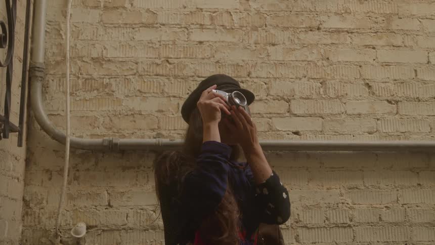Young female adult wearing a black hat and black dress smiling while taking pictures of her surroundings during a tourist site visit at midday