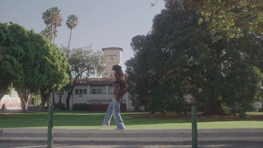 Young woman walking excitedly on a sidewalk in a suburban area with a lawn and trees in the background at midday