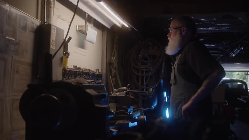 Man in an apron looks at the lit workbench in the workshop